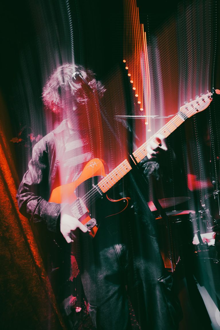South Australian musician performing live on stage playing an electric guitar captured with an artistic motion blur and red stage lighting effect.